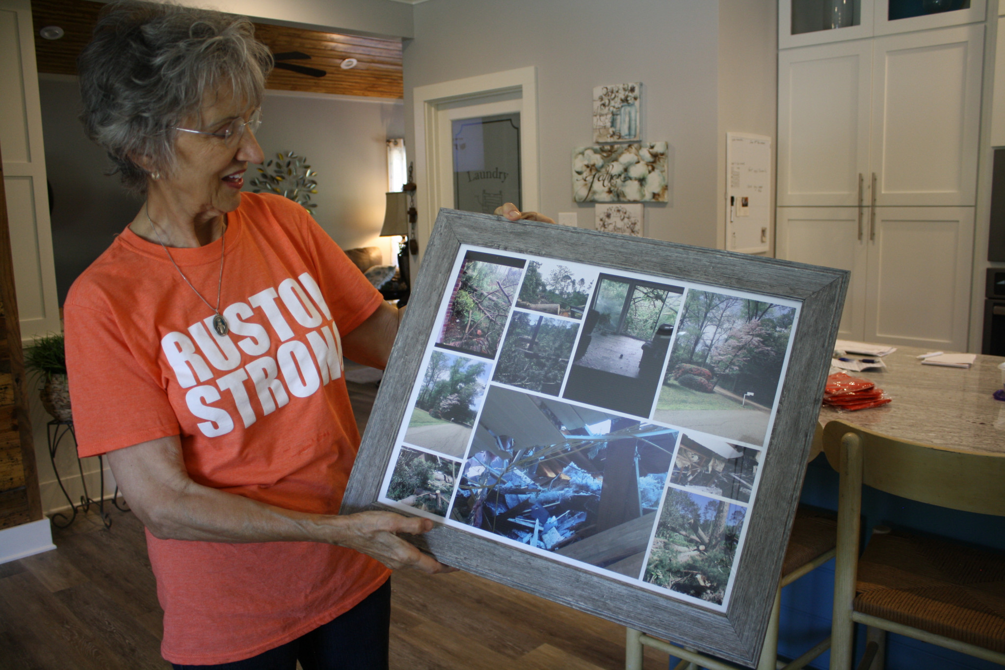 While standing in her remodeled Robinette Drive home, Mary Vidrine displays a collage of photos showing the damage the house sustained last year.